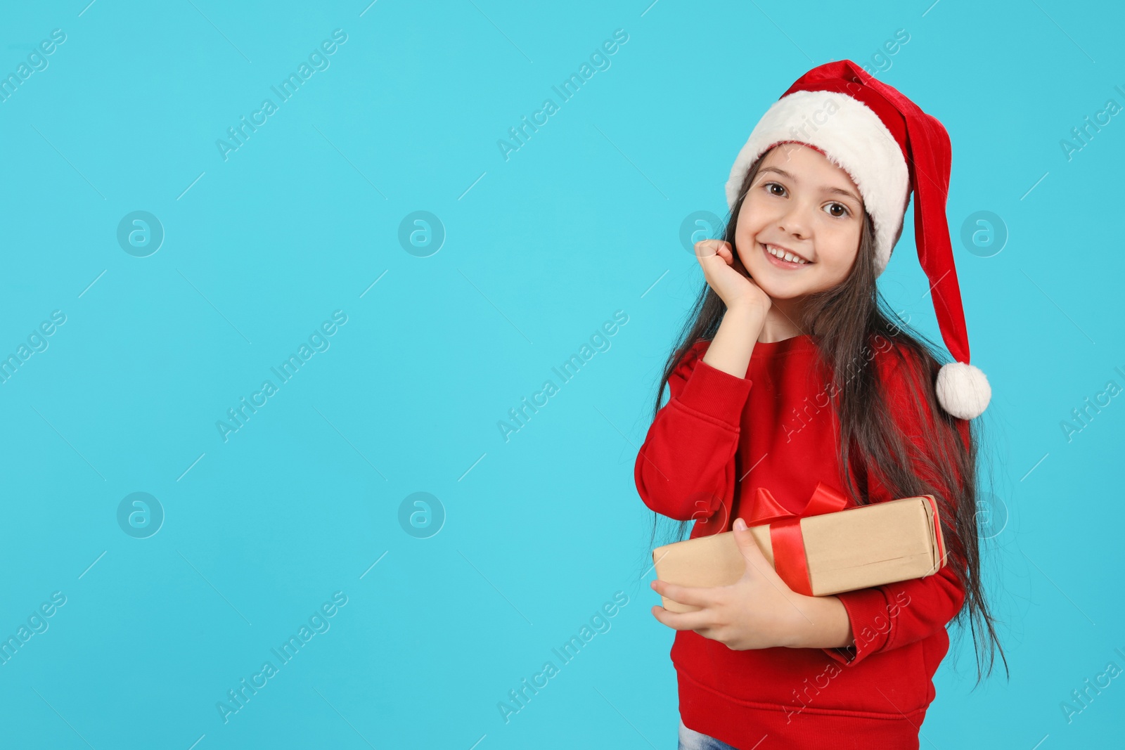 Photo of Cute little child in Santa hat with Christmas gift on color background