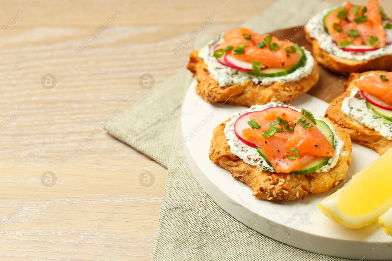 Photo of Tasty canapes with salmon, cucumber, radish and cream cheese on wooden table, space for text