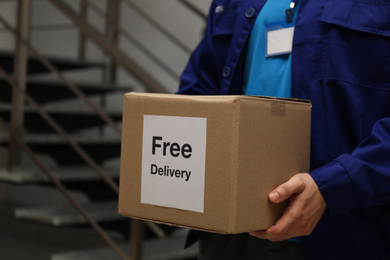 Courier holding parcel with sticker Free Delivery indoors, closeup