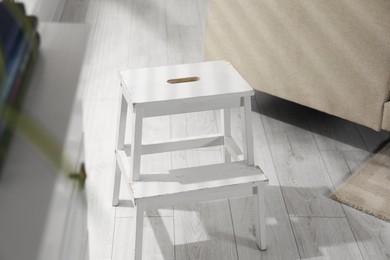 Photo of White compact ladder on wooden floor indoors