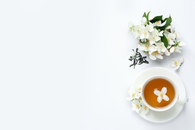 Cup of aromatic jasmine tea and fresh flowers on white background, top view. Space for text