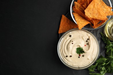 Photo of Delicious hummus with nachos and parsley on black table, top view. Space for text