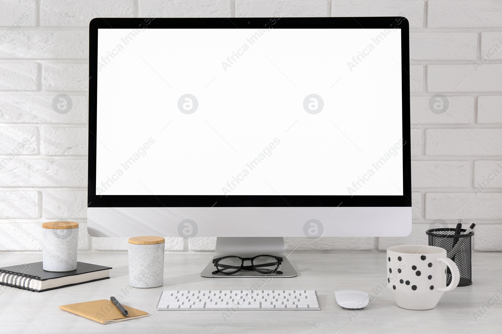 Photo of Office workplace with computer, cup and stationery on light table near white brick wall