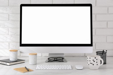 Office workplace with computer, cup and stationery on light table near white brick wall