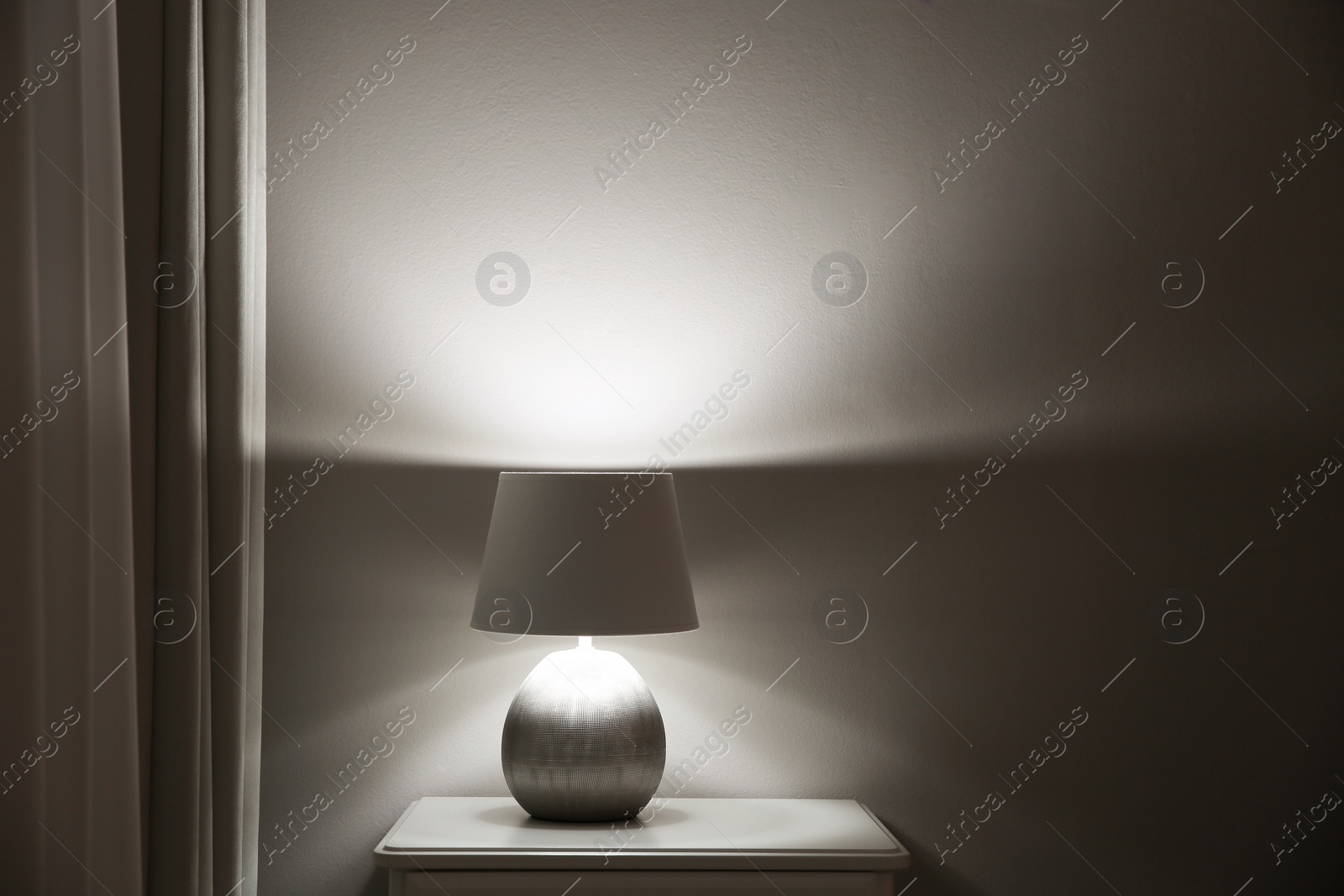 Photo of Wooden nightstand with modern lamp near light grey wall, space for text. Interior element