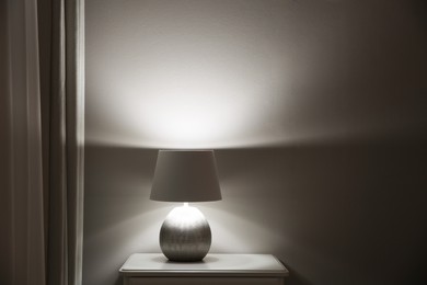 Photo of Wooden nightstand with modern lamp near light grey wall, space for text. Interior element