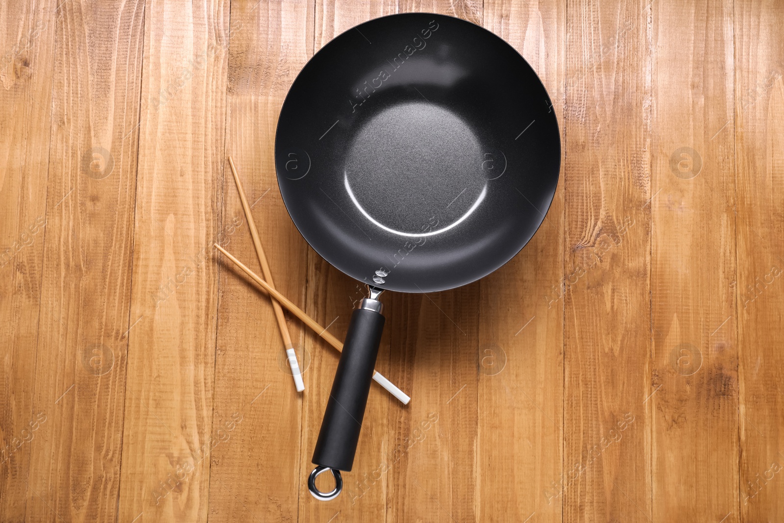 Photo of Empty iron wok and chopsticks on wooden table