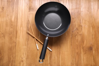 Photo of Empty iron wok and chopsticks on wooden table