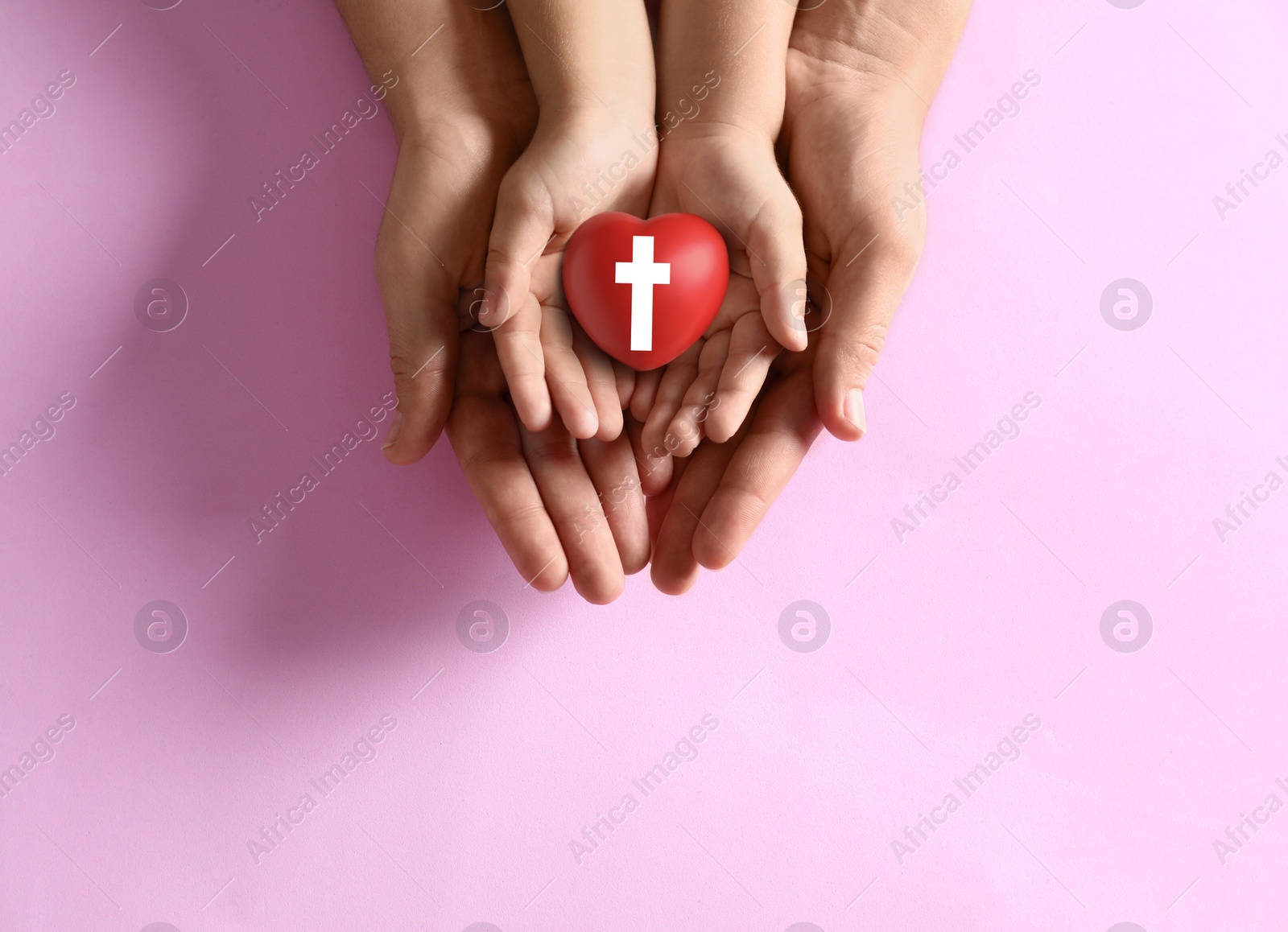 Image of Mother and her child holding heart with cross symbol on pink background, top view. Christian religion