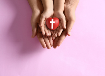 Mother and her child holding heart with cross symbol on pink background, top view. Christian religion