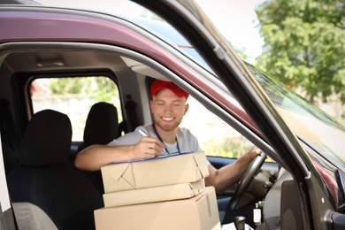 Young courier with parcels and clipboard in delivery car