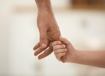 Photo of Father holding hands with his child indoors, closeup. Happy family