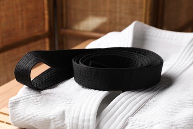 Photo of Martial arts uniform with black belt on table indoors, closeup