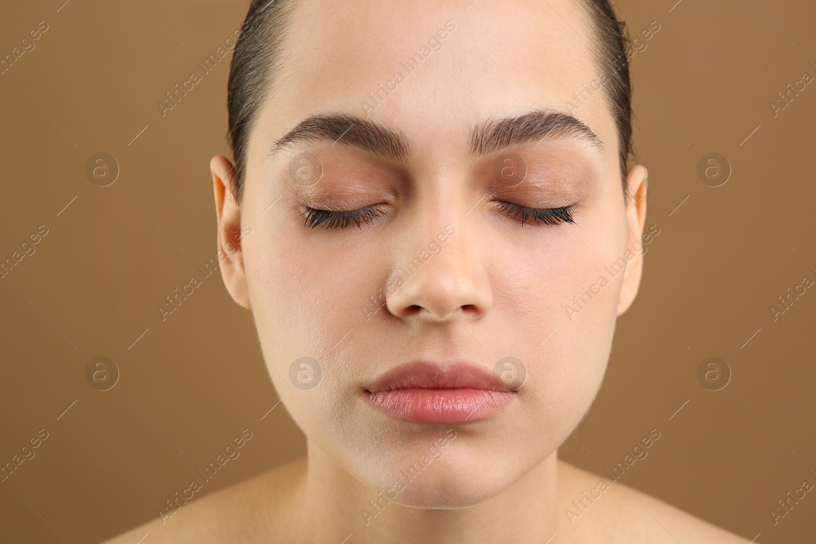 Photo of Young woman with perfect eyebrows on brown background, closeup