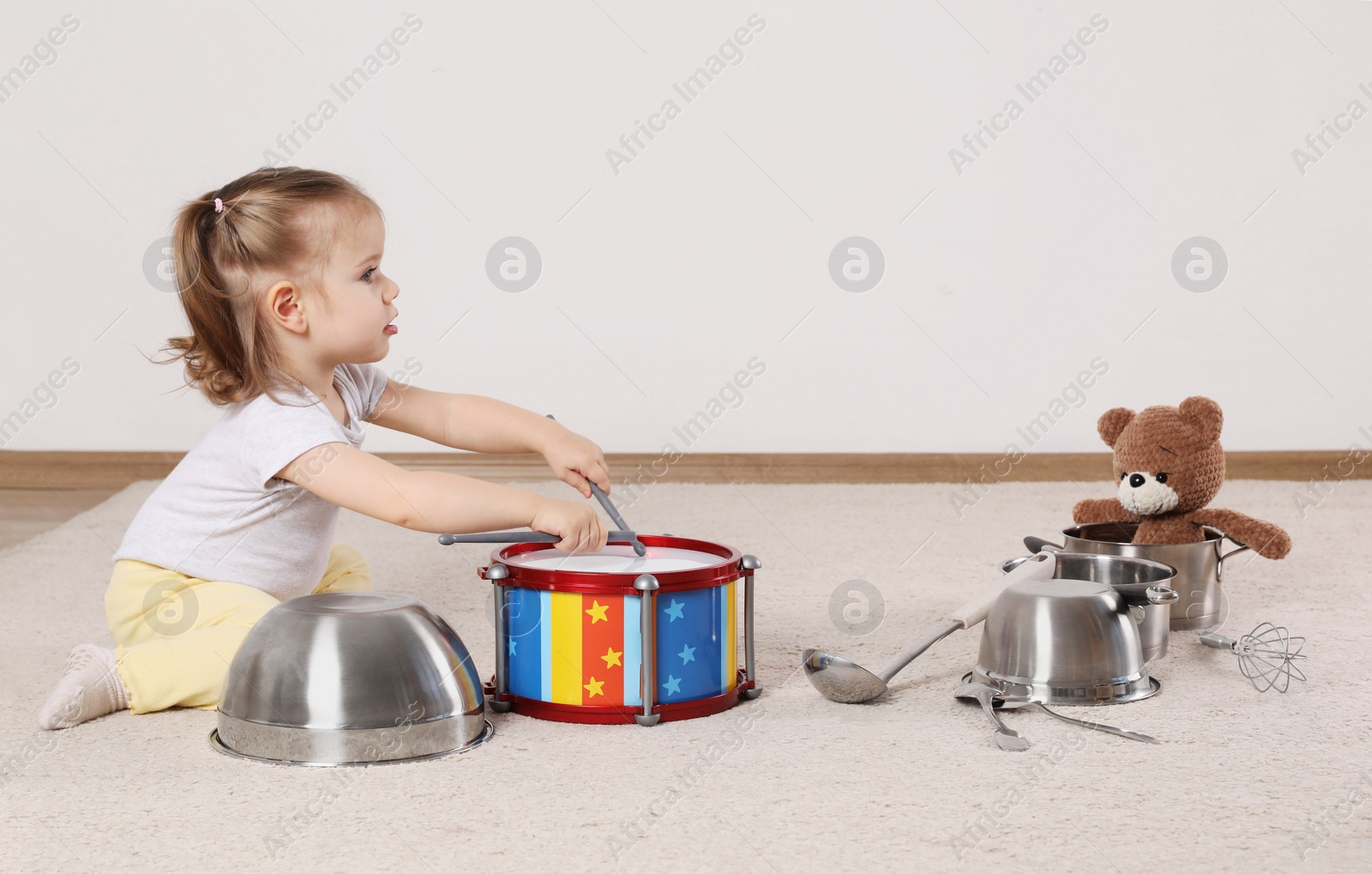 Photo of Cute little girl with cookware and toy drum at home