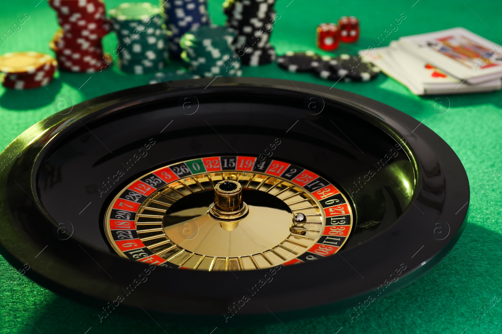 Photo of Roulette wheel with ball, playing cards and chips on green table, closeup. Casino game