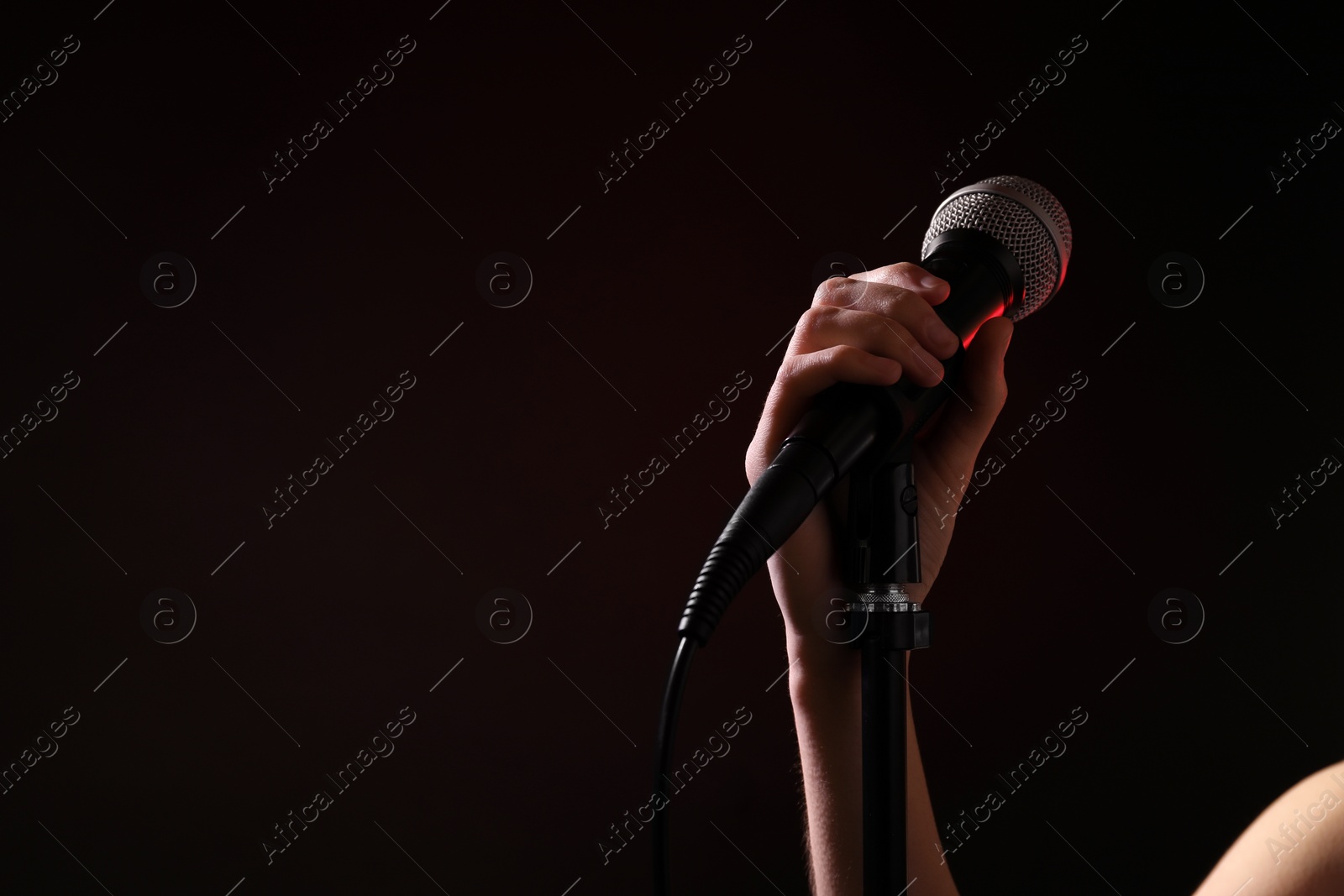 Photo of Woman holding microphone on black background, closeup. Space for text