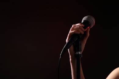 Woman holding microphone on black background, closeup. Space for text