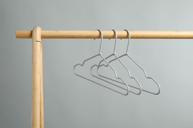 Photo of Empty clothes hangers on wooden rack against grey background