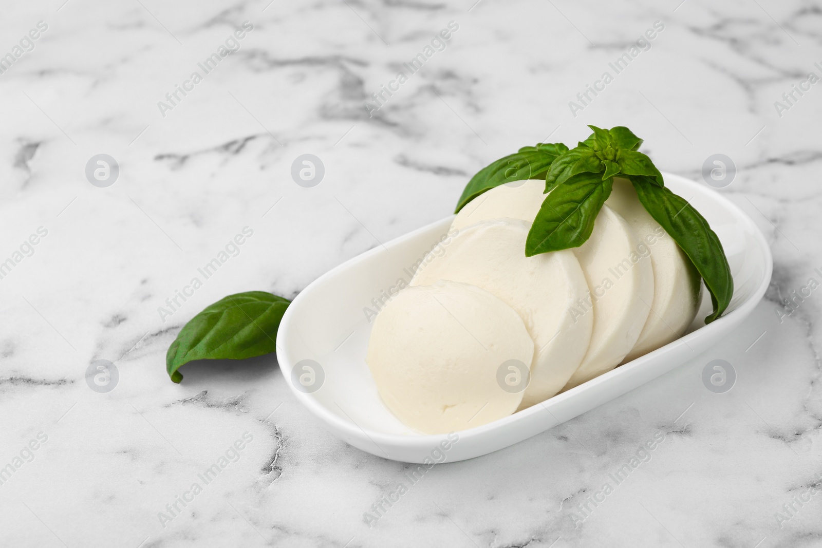 Photo of Plate with tasty mozzarella slices and basil leaves on white marble table. Space for text