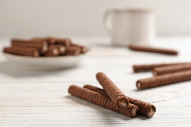 Photo of Delicious chocolate wafer rolls on white wooden table. Sweet food