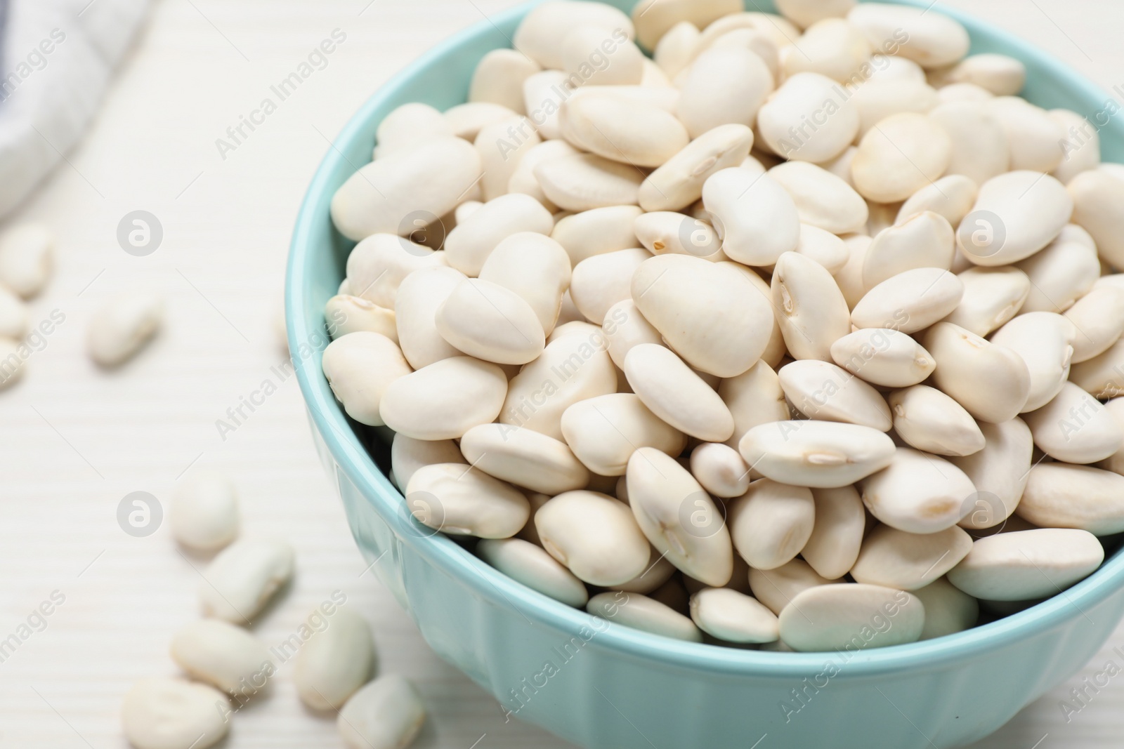 Photo of Raw beans and bowl on white table, closeup