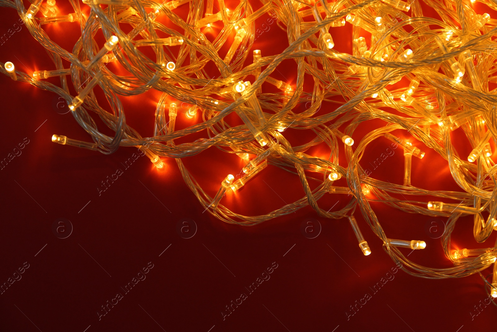 Photo of Glowing Christmas lights on red background, top view