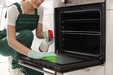 Photo of Professional janitor cleaning oven with sponge in kitchen, closeup