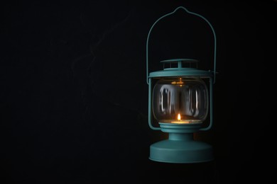 Photo of Vintage lantern with burning candle on black background. Space for text