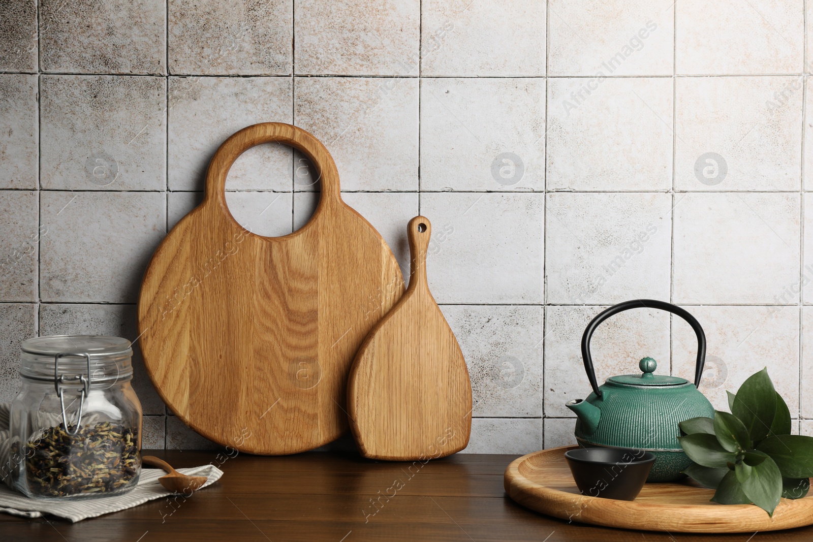 Photo of Wooden cutting boards, kettle and tea on table near tiled wall. Space for text