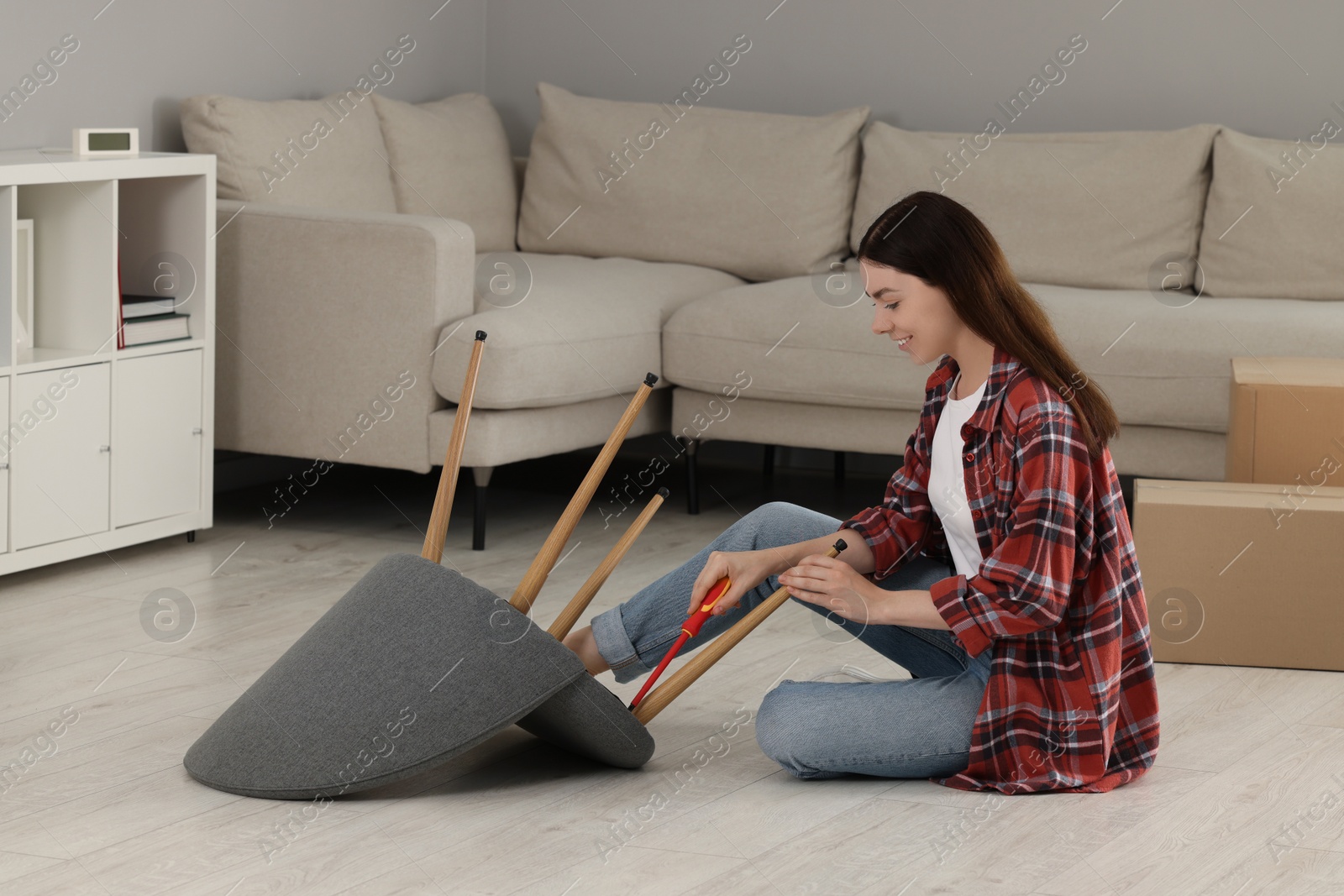 Photo of Young woman with screwdriver assembling armchair on floor at home