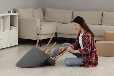 Photo of Young woman with screwdriver assembling armchair on floor at home