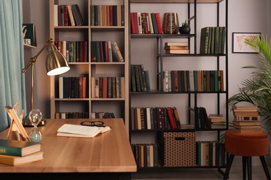 Photo of Wooden table and collection of different books on shelves in home library