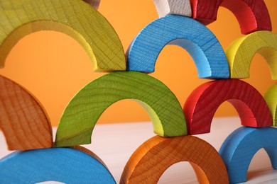 Colorful wooden pieces of educational toy on light table against orange wall, closeup. Motor skills development