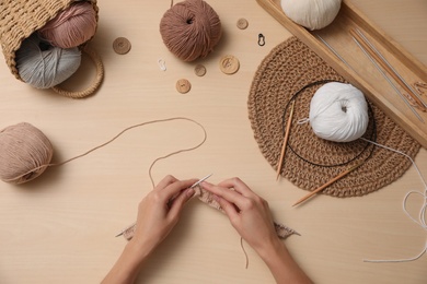 Woman knitting with threads at wooden table, top view. Engaging hobby