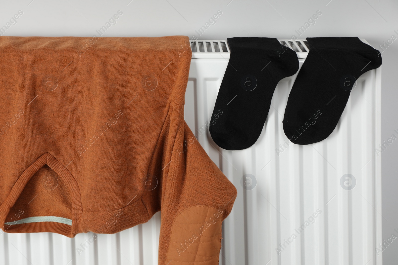 Photo of Brown pullover and black socks hanging on white radiator indoors