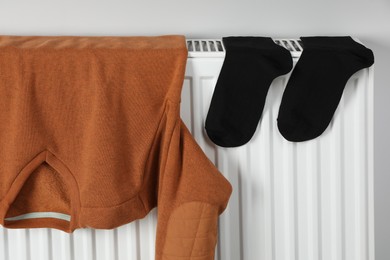 Photo of Brown pullover and black socks hanging on white radiator indoors