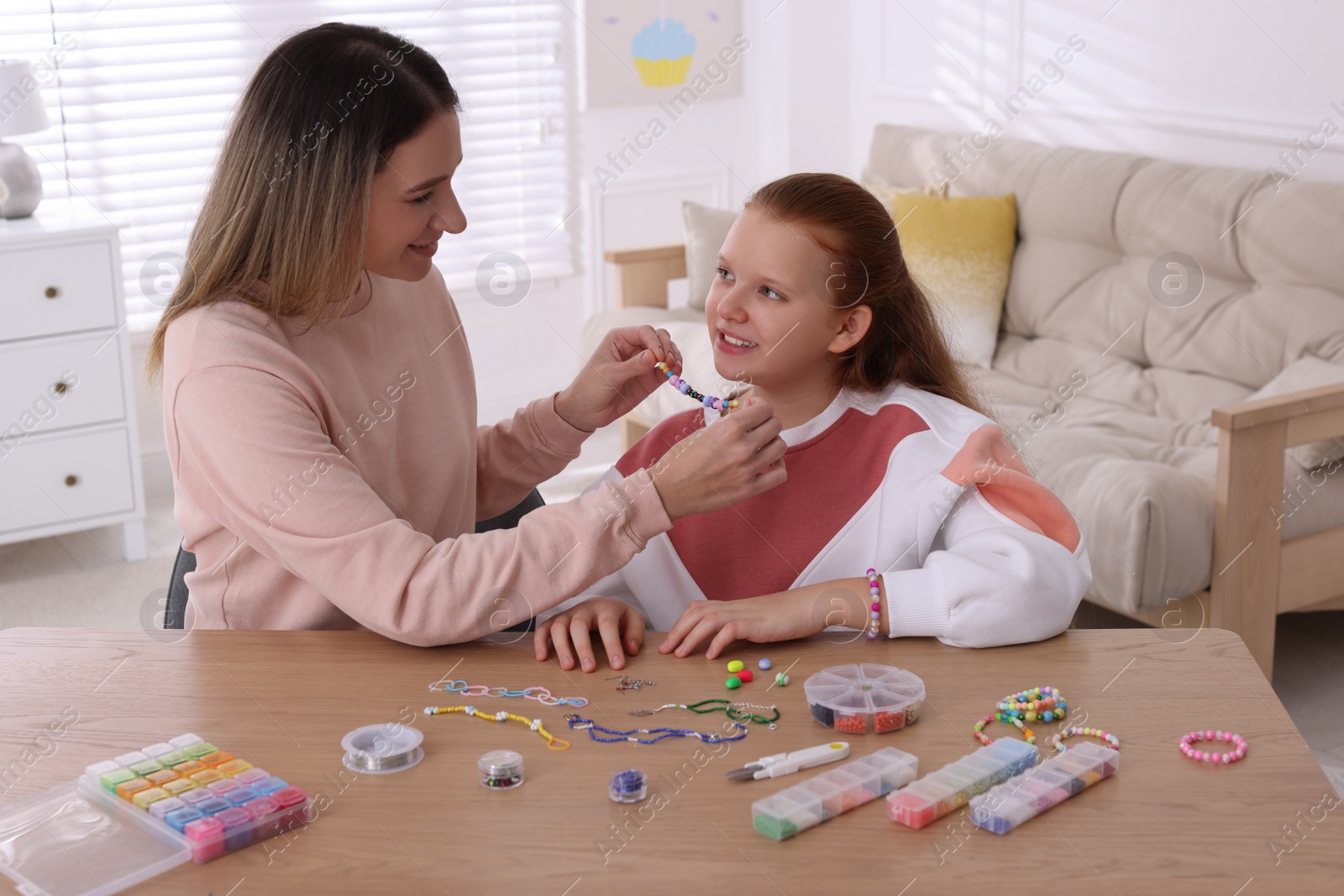 Photo of Happy mother with her daughter making beaded jewelry at home