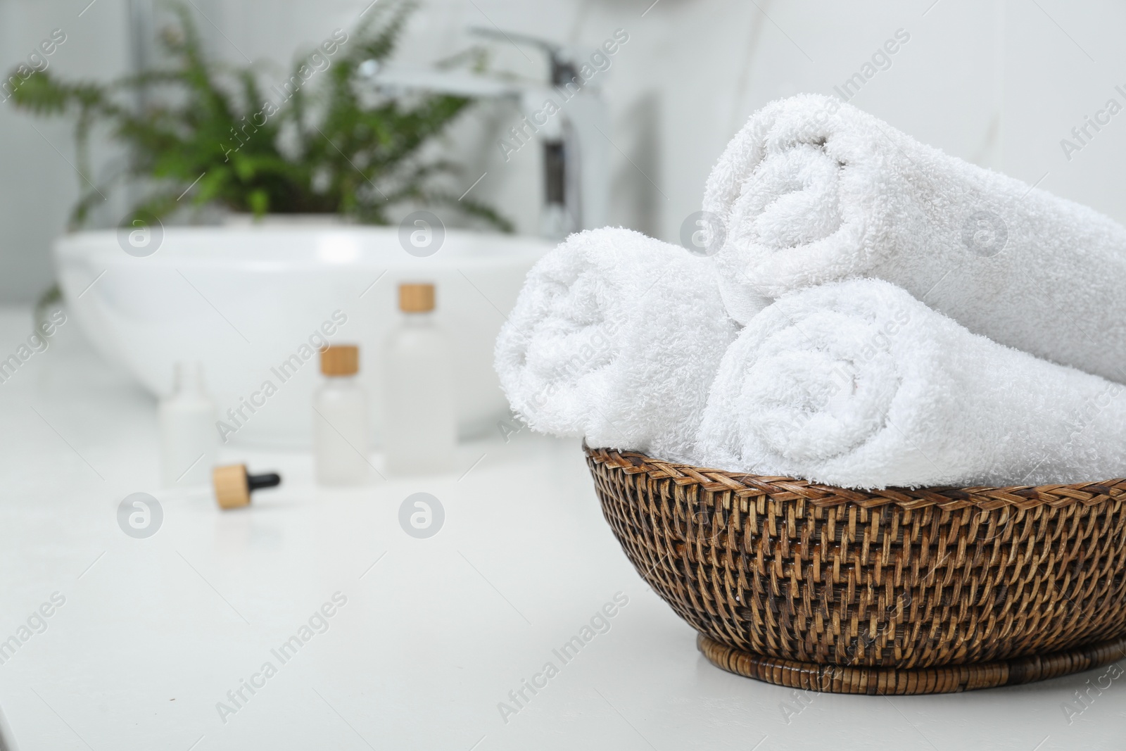 Photo of Rolled bath towels in wicker bowl indoors, space for text