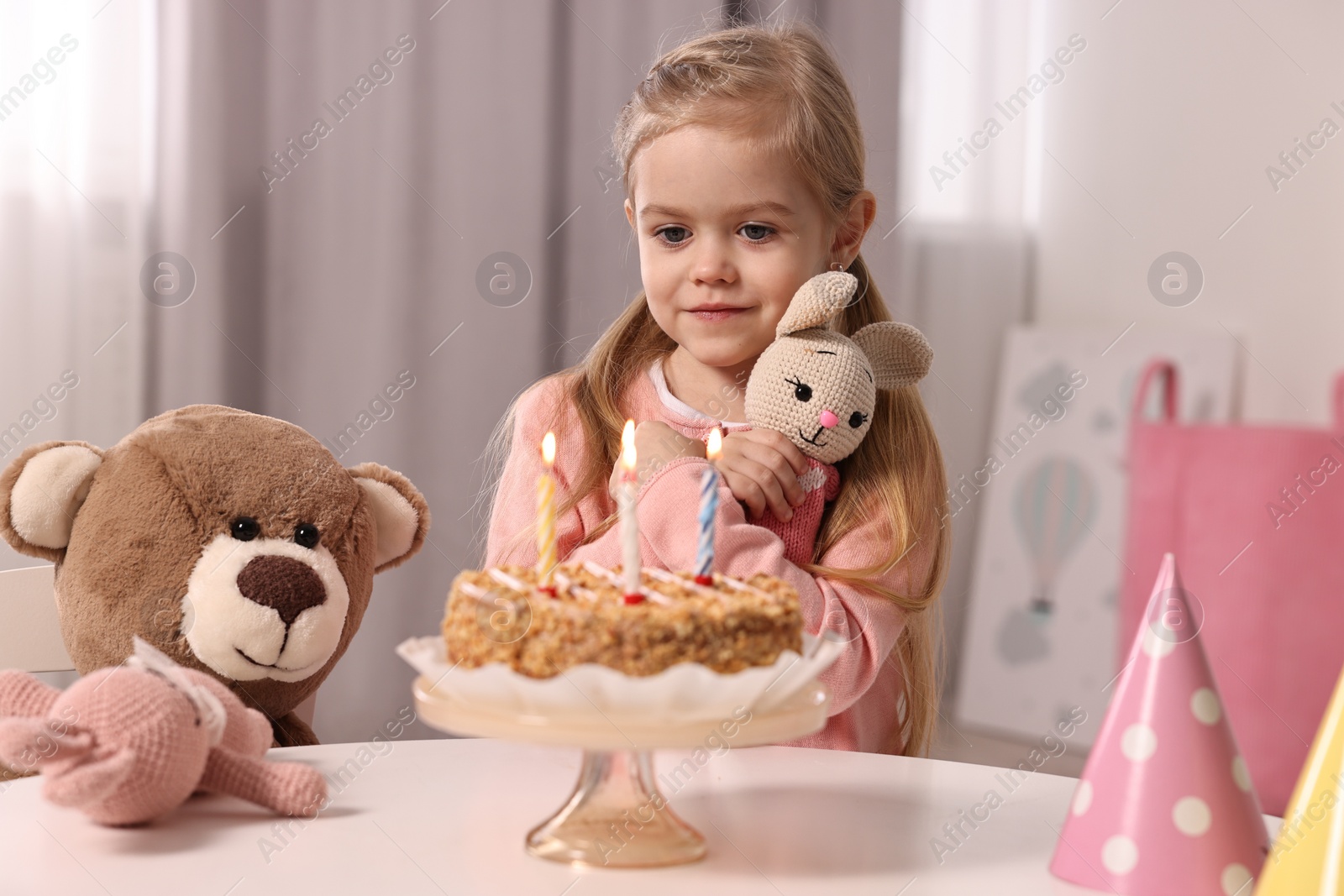 Photo of Cute girl with birthday cake and toys at table indoors