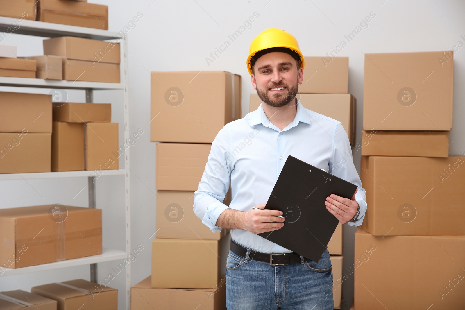 Photo of Young man with clipboard near cardboard boxes at warehouse