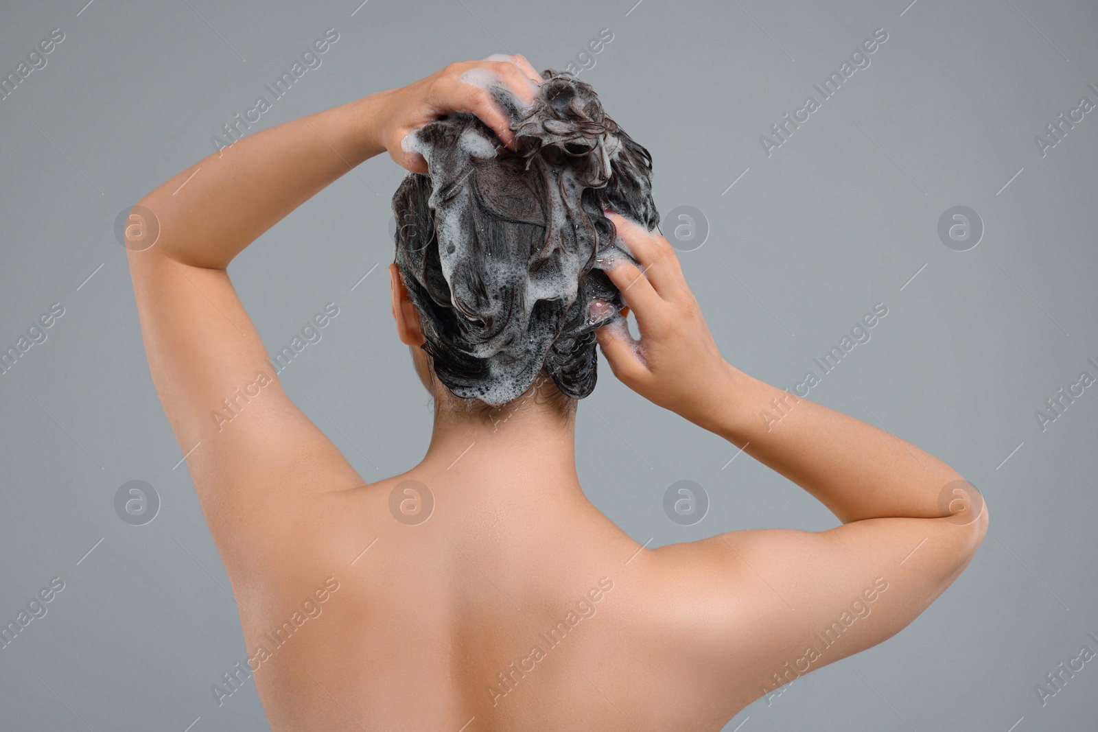 Photo of Woman washing hair on grey background, back view