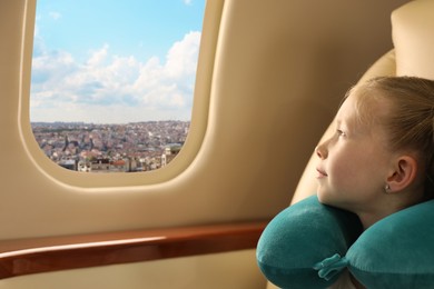 Image of Cute little girl with travel pillow looking out of window in airplane during flight