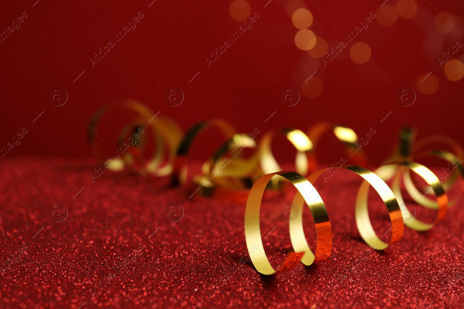 Photo of Shiny golden serpentine streamers on red table against blurred lights. Space for text