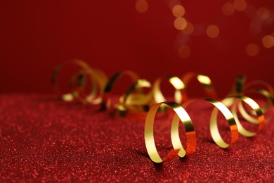 Photo of Shiny golden serpentine streamers on red table against blurred lights. Space for text