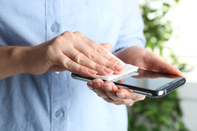 Photo of Woman cleaning smartphone with paper napkin indoors, closeup