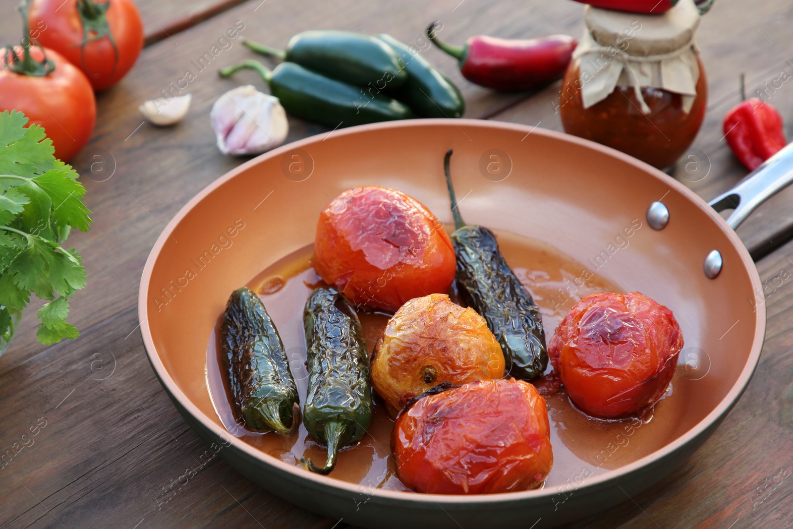 Photo of Frying pan with ingredients for salsa sauce on wooden table