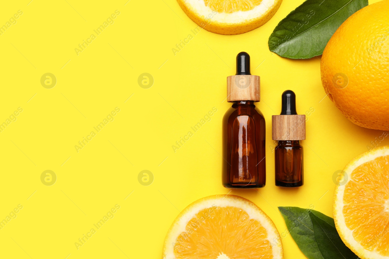 Photo of Bottles of citrus essential oil and fresh oranges on yellow background, flat lay. Space for text