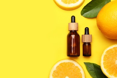 Photo of Bottles of citrus essential oil and fresh oranges on yellow background, flat lay. Space for text