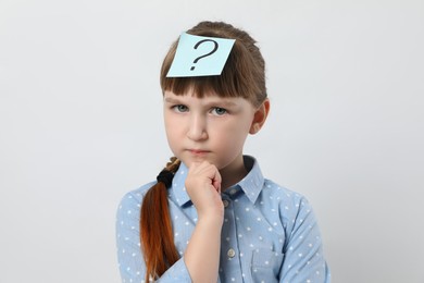 Photo of Pensive girl with question mark sticker on forehead against white background